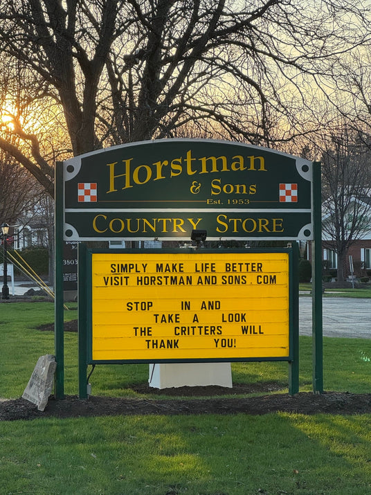 Sign for Horstman & Sons Country Store with a yellow message board in front of leafless trees.